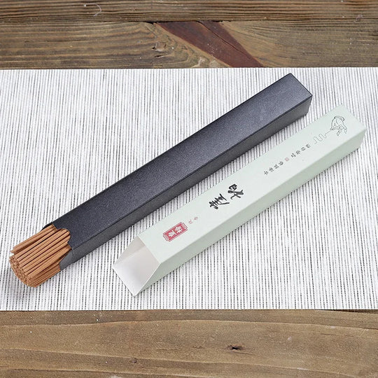 Flat lay of single sandalwood incense box with partially revealed incense sticks on wood surface