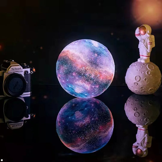 3D-printed moon lamp glowing beside camera and decorative spheres.